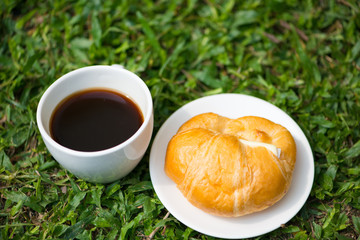 A white cup and black coffee with Croissant with cheese on nature floor