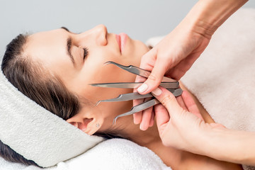 Cosmetologist holds tweezers for eyelash extensions next to face of young woman, close up.