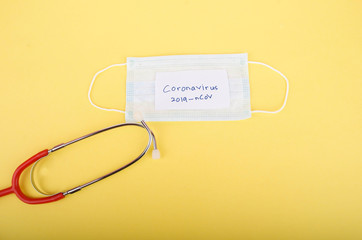 Coronavirus 2019-nCoV text on paper with protective mask and stethoscope on yellow background. Selective focus
