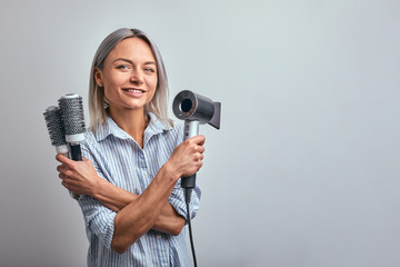 Attractive woman blonde hairdresser with professional tool posing on camera, gray background. Copy space, advertising banner, beauty concept.