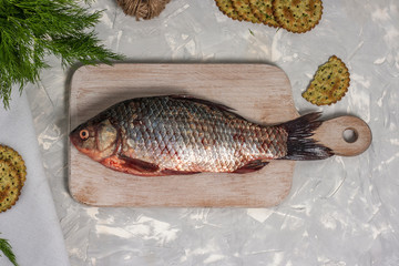 Fresh crucian fish lies on a white wooden cutting board on a light gray background. Top view