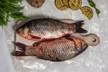 Two fresh crucian fish lies on a white wooden cutting board on a light gray background. Top view