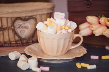 Fototapeta na wymiar colorful marshmallows in a cup and saucer on a wooden table, tulips