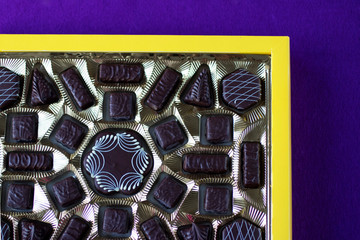 Assorted chocolates in yellow box on  purple background.