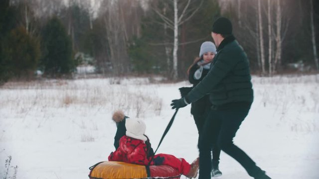 Family running and playing outdoors near the forest - man rolls his kids on the inflatable sled
