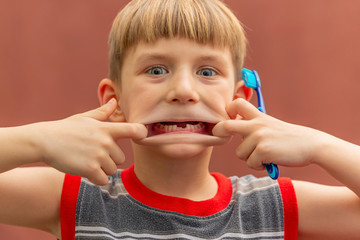 A child with a toothbrush in his hand shows a toothless mouth swelling his cheeks.