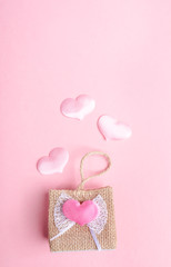 Small decorative wicker handbag and three flying out of it pink hearts on pink background. Valentine's day concept.