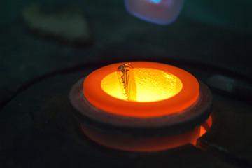 closeup of gold bar melting in liquid metal in furnace, glowing red-hot