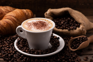 Cappuccino and croissant with coffee beans close up