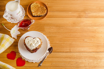 Fritters, pancakes in the form of hearts with jam and whipped cream with copy space on a light wooden background with red hearts, romantic breakfast for Valentine's Day. Mothers Day. Cooking