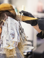 Master in black gloves dyes hair to woman at hairdresser