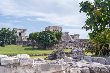 Fototapeta na wymiar Ruins of ancient Tulum. Architecture of ancient maya. View with temple and other old buildings, houses. Blue sky and lush greenery of nature. travel photo. Wallpaper or background. Yucatan. Mexico.