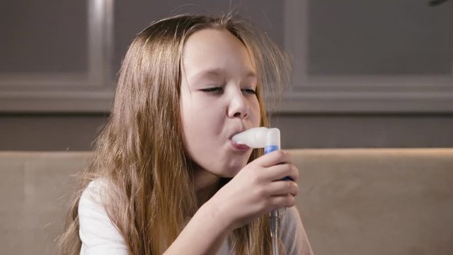 Cute blonde girl baby breathes through a tube of steam with medication from an inhaler. Prevention of increasing immunity, fighting viruses at home