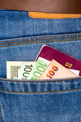Closeup of various countries hundred banknotes and EU passport peeking out of blue jeans back pocket