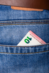 Closeup of five and ten Euro banknote peeking out of blue jeans back pocket