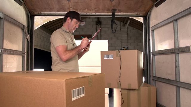 Courier / Delivery man scanning parcels / packages in the back of a  shipping / freight truck. He has using a Clipboard