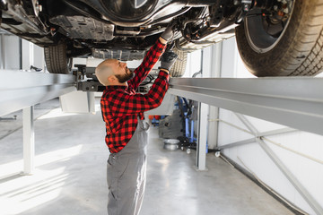 Auto mechanic working underneath a lifted car. Auto mechanic working in garage. Repair service.