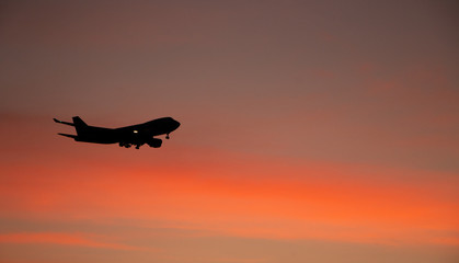Silhouette of big airplane on beautiful orange sunset background, fast aerial transport, traveling and voyage concept