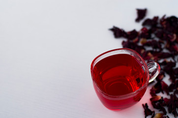 A Cup of red tea on a white table. Hibiscus brewed in a transparent Cup. Dried hibiscus brewed with boiling water.