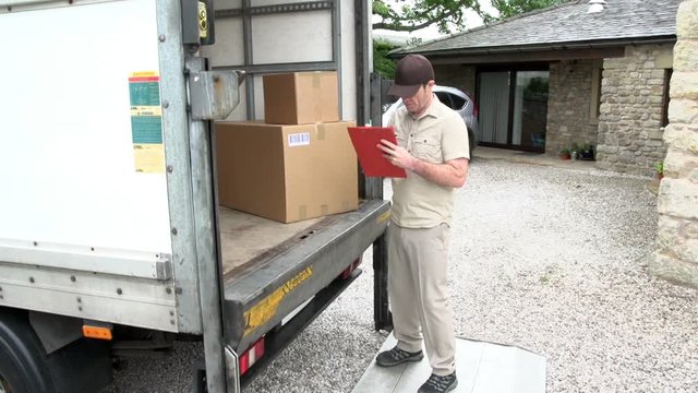 Courier / Delivery man writes on clipboard with parcel in the back of a  shipping / freight truck. Logistics. At home / House