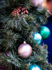 Christmas toys close-up on the branches of green plastic spruce. Macro shot of Christmas tree accessories. Mock up for holiday card background. Copy space on blurred bokeh