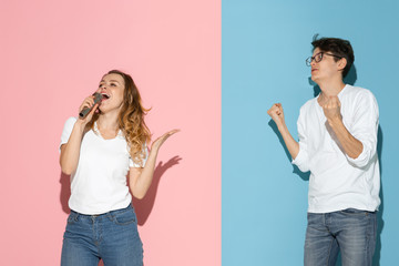 She's singing, he's shocked. Young and happy man and woman in casual clothes on pink, blue bicolored background. Concept of human emotions, facial expession, relations, ad. Beautiful caucasian couple.