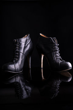 Black women's ankle boots on a black surface reflecting the ankle boots. The photo is taken in a photo studio with flash light illuminating the boots and on a black background