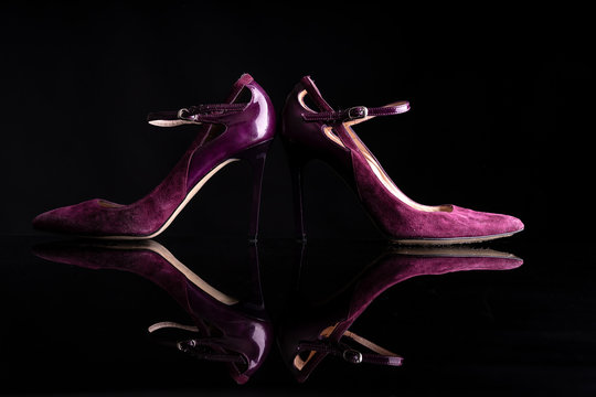 pair of purple velvet shoes on black background resting on black surface reflecting shoes