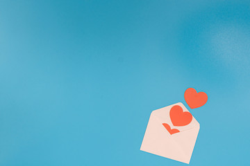 A few red hearts pop out from a light pink envelope on a blue background