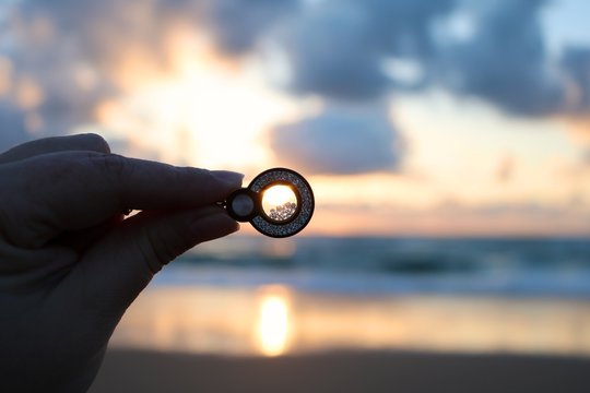 Cropped Hand Of Woman Holding Locket Against Sky