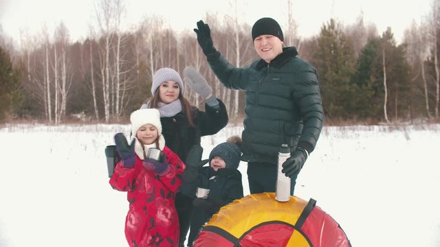Family standing outdoors holding termos and cups with tea - waving hands