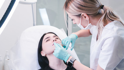Beautician hands making botox injection in female lips. The doctor cosmetologist makes lip...