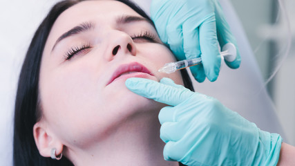 Beautician hands making botox injection in female lips. The doctor cosmetologist makes lip augmentation procedure.