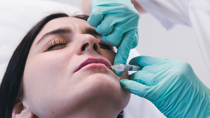 Beautician hands making botox injection in female lips. The doctor cosmetologist makes lip augmentation procedure.