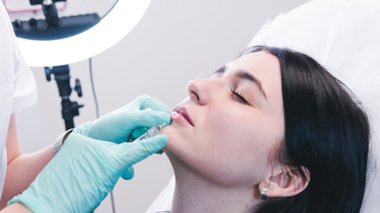 Beautician hands making botox injection in female lips. The doctor cosmetologist makes lip...