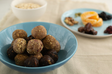 Energy balls of oatmeal with nuts, dates, pumpkin seeds, cranberries, prunes and tangerines in a blue bowl with on a light background.