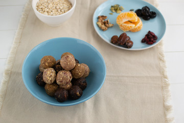Energy balls of oatmeal with nuts, dates, pumpkin seeds, cranberries, prunes and tangerines in a blue bowl with on a light background.