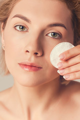 woman with short blond hair wipes her face with a cotton pad. Skin care concept