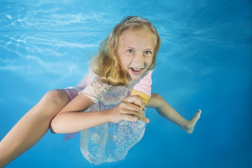 Girl in white dress eating ice cream underwater. Young beautiful girl poses underwater in the pool.