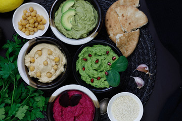 Colorful hummus bowls background. Different kinds of dips. Traditional hummus, herbs hummus, beetroot hummus, spread. Assorted meze and dips with crispy pita. Space for text. Meze and snacks concept
