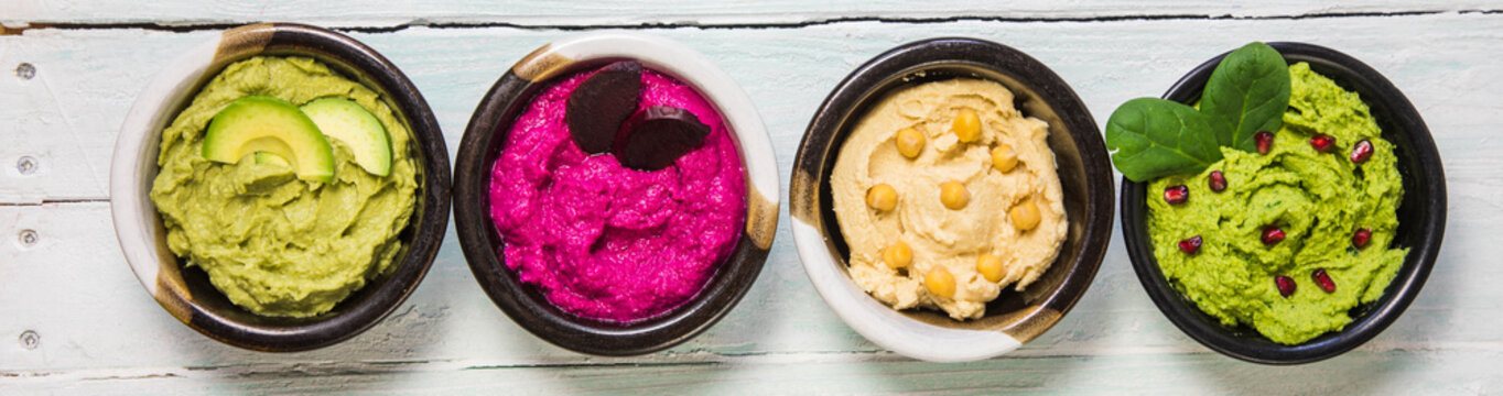 Colorful hummus bowls background. Different kinds of dips. Traditional hummus, herbs hummus, beetroot hummus, spread. Assorted meze and dips with crispy pita. Space for text. Meze and snacks concept
