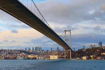 Bottom view of Bosphorus Bridge (also known as 15 July Martyrs Bridge) over strait. Beylerbeyi district with Beylerbeyi Mosque in the background. Beautiful landscape on a winter sunny day