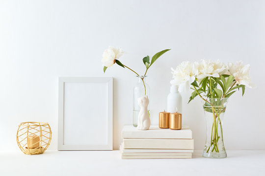 Home interior with decor elements. White frame, white peonies in a vase, interior decoration