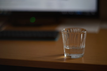 Half a glass of water on a table with a keyboard and monitor.