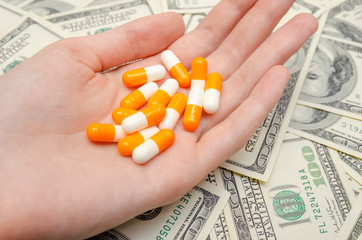 Orange and white pills in hand against the background of dollars. Lots of psychedelic pills. Drug addiction and crime