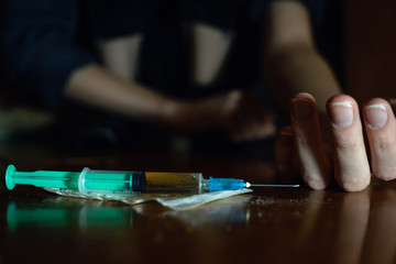 Drug addict makes a syringe injection into the vein of the hand close up on the floor in the dark