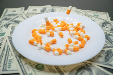 white plate with orange-and-white tablets on the table with dollar bills. Photos of falling tablets in a plate, freezing photos