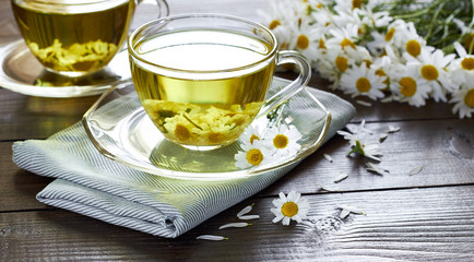 Chamomile herbal tea with flower buds nearby on wooden table with textile and camomile bouquet, closeup, copy space, healthy herbal drinks and natural healer concept