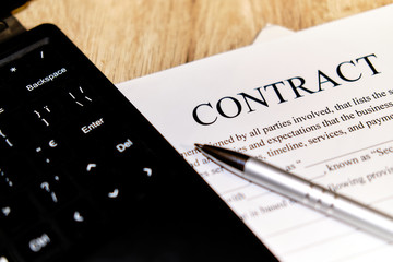 A pen for the signature of the Contract. Glasses and tablet on a wooden table