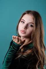 Beautiful young woman in a green dress blowing a kiss to somebody isolated on blue background